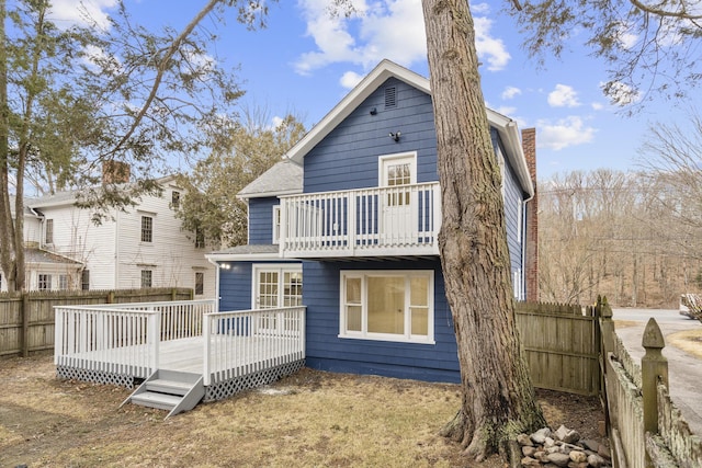 back of house featuring a deck, a chimney, a fenced backyard, and a balcony