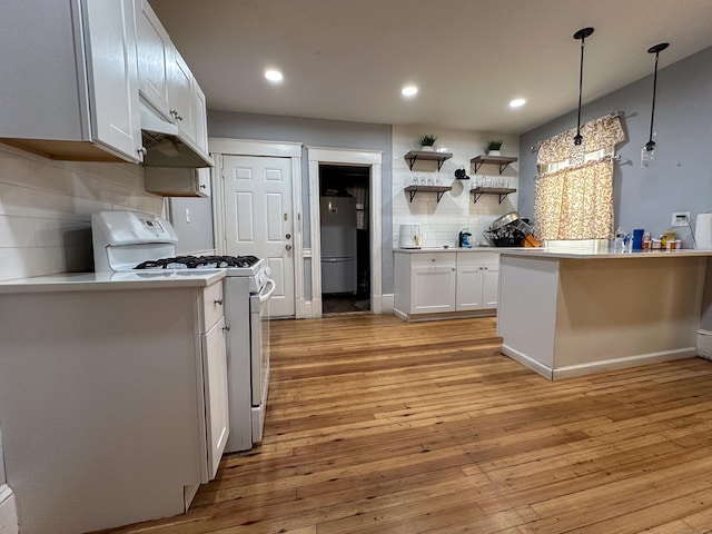 kitchen featuring light wood finished floors, backsplash, white gas stove, freestanding refrigerator, and white cabinetry