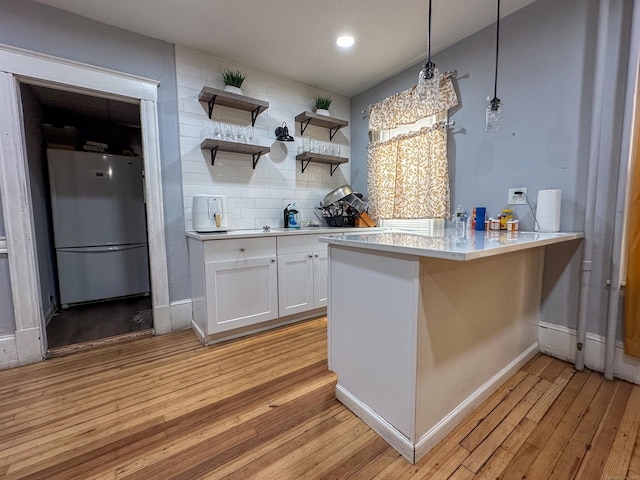 kitchen with light wood-type flooring, white cabinetry, tasteful backsplash, and freestanding refrigerator