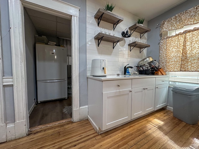 kitchen with backsplash, light countertops, freestanding refrigerator, light wood-style floors, and white cabinets