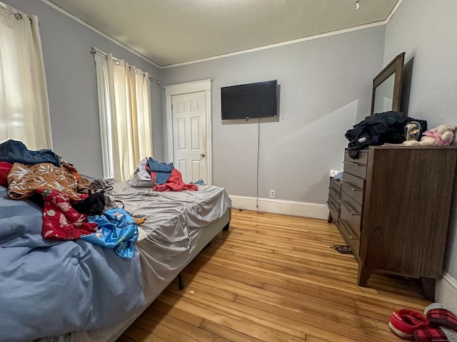 bedroom featuring light wood finished floors, baseboards, and ornamental molding