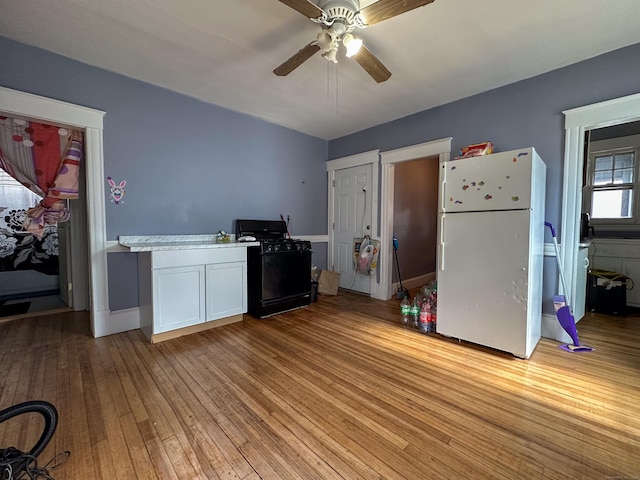 kitchen with black gas stove, freestanding refrigerator, light countertops, white cabinetry, and light wood-type flooring