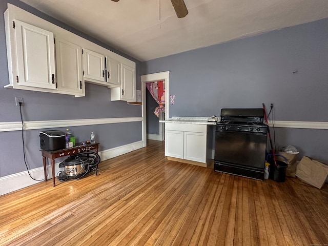 kitchen featuring hardwood / wood-style floors, gas stove, white cabinets, baseboards, and ceiling fan