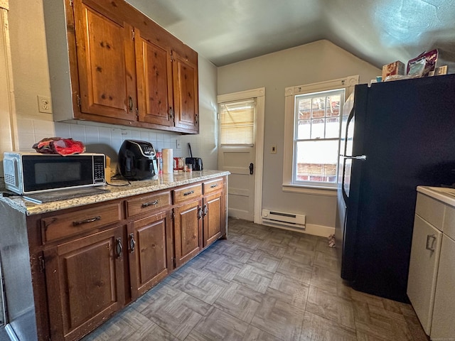 kitchen with brown cabinets, a baseboard heating unit, backsplash, freestanding refrigerator, and lofted ceiling