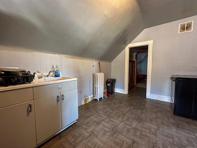 kitchen featuring visible vents, a sink, radiator heating unit, light countertops, and lofted ceiling