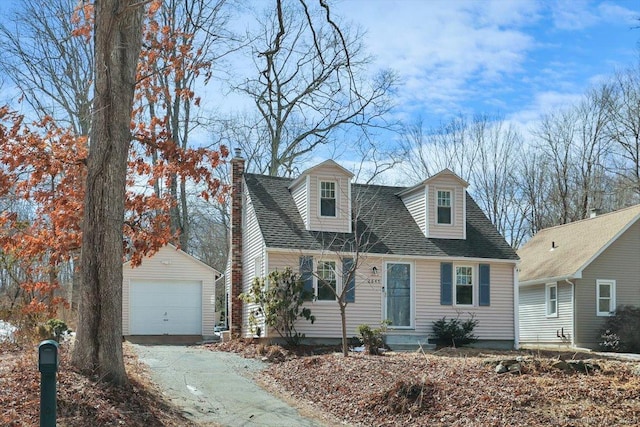 cape cod-style house with driveway, a garage, a shingled roof, a chimney, and an outdoor structure