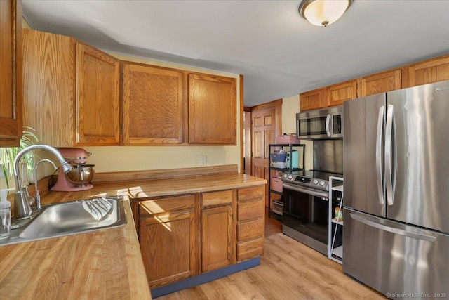 kitchen featuring light wood-style flooring, appliances with stainless steel finishes, brown cabinets, and a sink