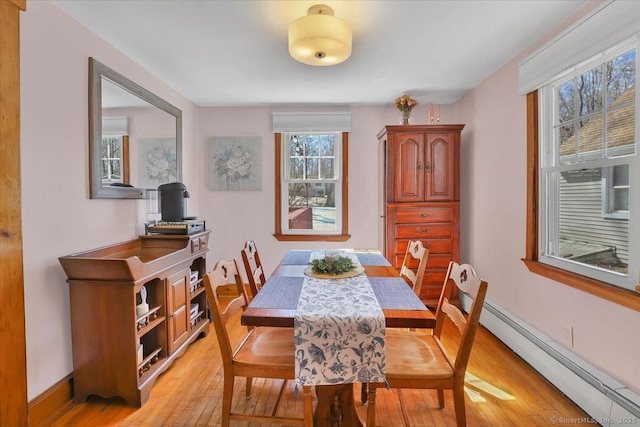 dining area with a baseboard heating unit, light wood-type flooring, and baseboards