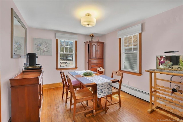 dining space with a baseboard heating unit, light wood-style flooring, and baseboards