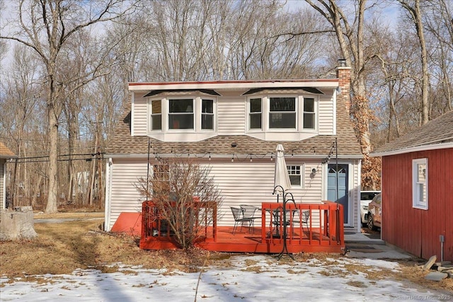 view of front of house with roof with shingles, a chimney, and a wooden deck