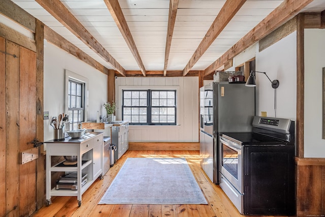 kitchen with wooden walls, stainless steel electric stove, freestanding refrigerator, beamed ceiling, and light wood-type flooring