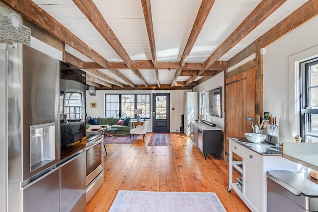 kitchen with light wood-type flooring, beam ceiling, white cabinetry, stainless steel appliances, and a healthy amount of sunlight