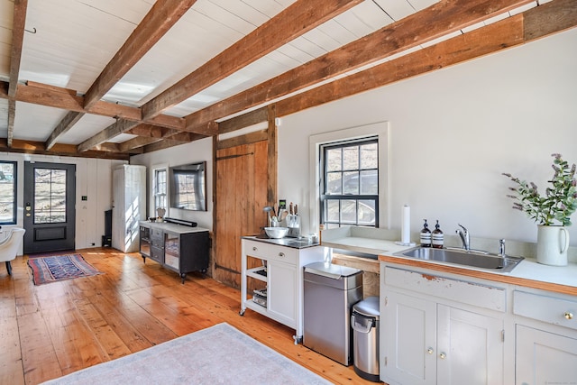 kitchen with beamed ceiling, plenty of natural light, light wood-style floors, and a sink