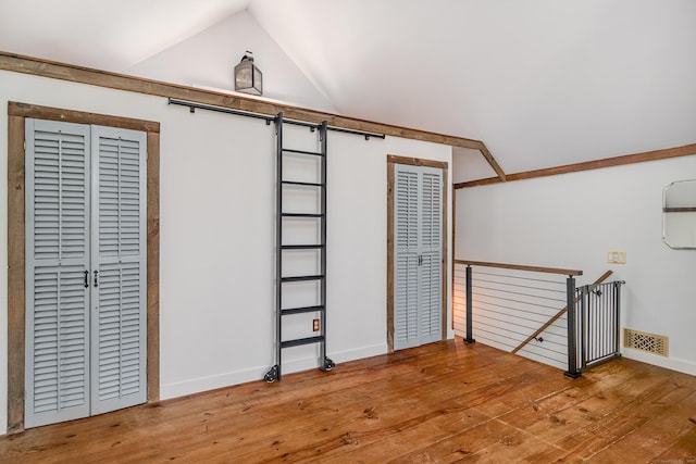 bonus room featuring hardwood / wood-style floors, lofted ceiling, a barn door, and visible vents