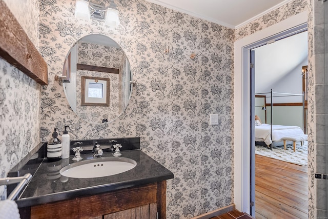 ensuite bathroom with vanity, wood finished floors, wallpapered walls, ornamental molding, and connected bathroom