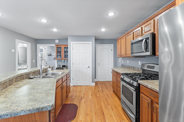 kitchen with brown cabinetry, recessed lighting, a sink, light wood-style floors, and appliances with stainless steel finishes