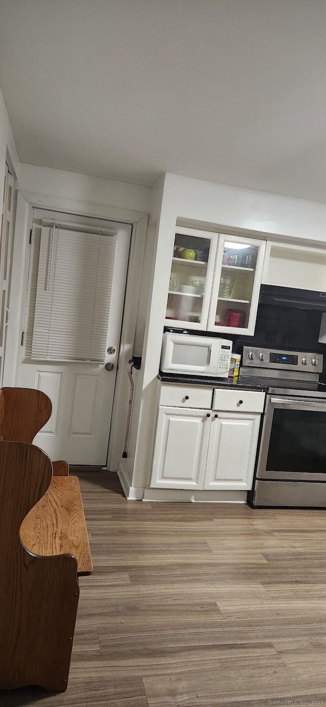 kitchen featuring white microwave, white cabinets, stainless steel electric range, light wood finished floors, and dark countertops