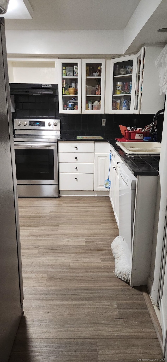 kitchen featuring stainless steel appliances, dark countertops, glass insert cabinets, white cabinets, and wood finished floors