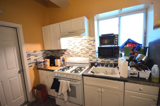 kitchen with a sink, under cabinet range hood, gas range gas stove, backsplash, and white cabinetry