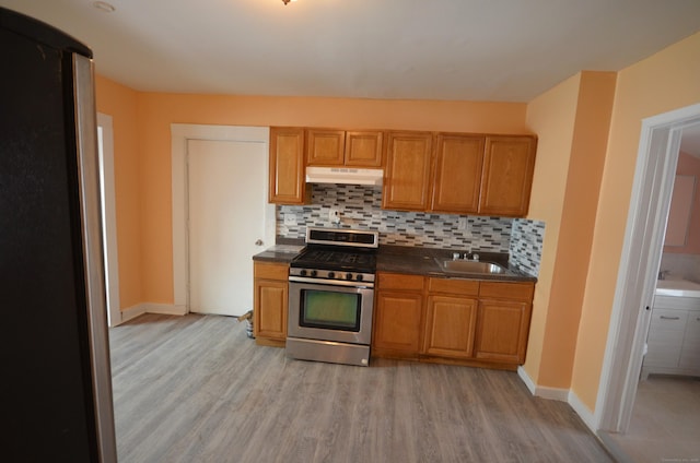 kitchen featuring dark countertops, backsplash, under cabinet range hood, appliances with stainless steel finishes, and a sink