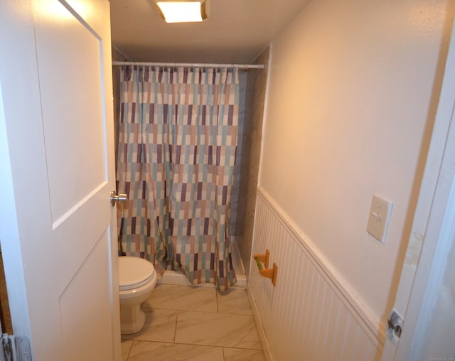 bathroom with a shower with shower curtain, toilet, marble finish floor, and wainscoting