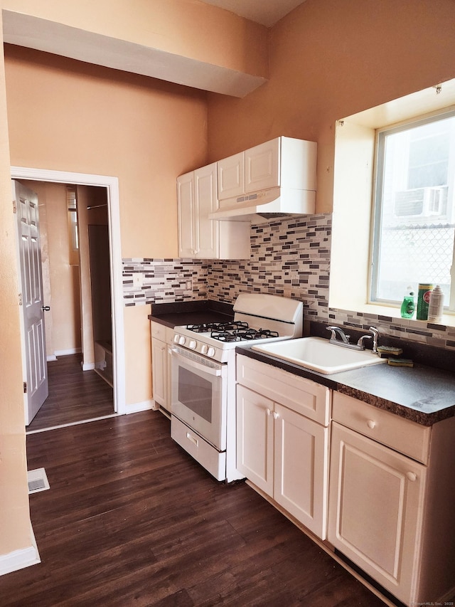 kitchen featuring dark countertops, dark wood-type flooring, white gas range, decorative backsplash, and a sink