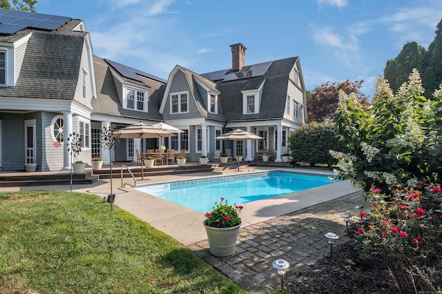 3 Sea Meadows Ln, Waterford, CT 06385 - rear view of house featuring a patio, roof mounted solar panels, a gambrel roof, an outdoor pool, and a chimney