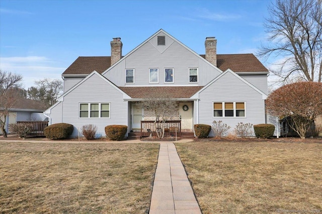 rear view of house featuring covered porch, a yard, roof with shingles, and a chimney