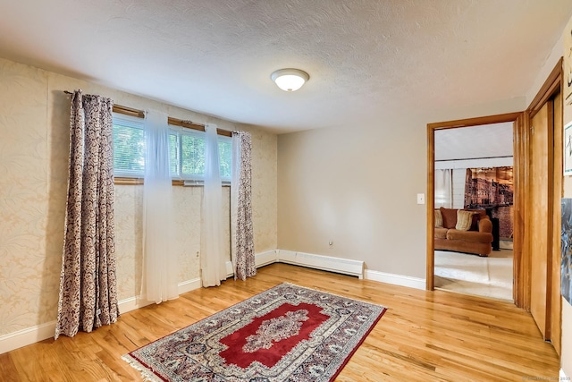 interior space featuring a textured ceiling, a baseboard radiator, wood finished floors, and baseboards