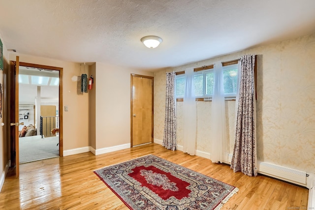 foyer featuring a baseboard radiator, a textured ceiling, baseboards, and wood finished floors