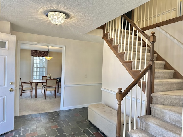 staircase with a textured ceiling, carpet floors, baseboards, and stone tile floors