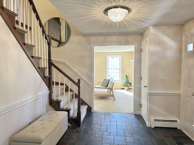 entrance foyer featuring a textured ceiling, a baseboard radiator, stone tile floors, baseboards, and stairway