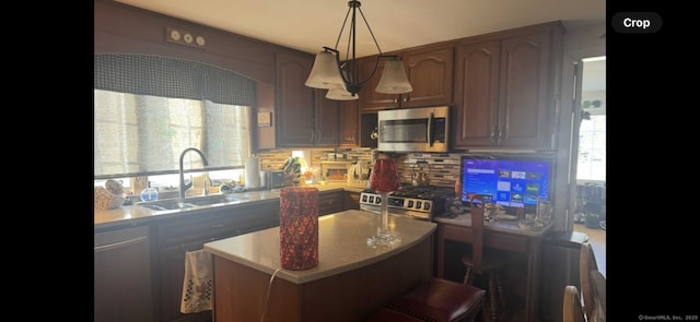 kitchen with tasteful backsplash, a kitchen island, appliances with stainless steel finishes, hanging light fixtures, and a sink