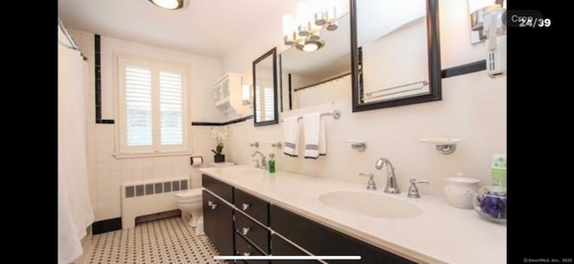 full bath with a sink, radiator, double vanity, and toilet