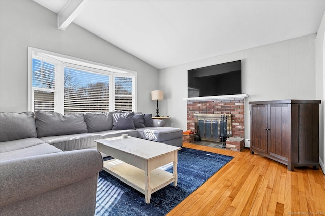 living area with a brick fireplace, vaulted ceiling with beams, and light wood-type flooring