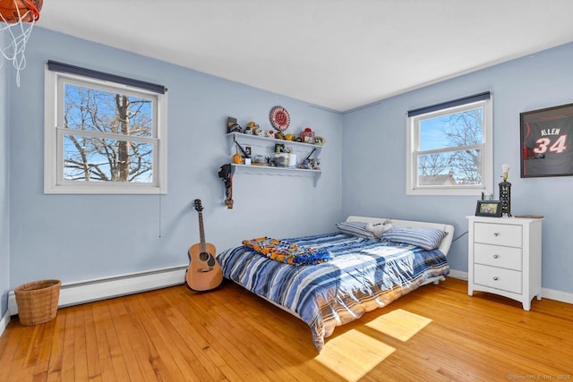 bedroom with a baseboard heating unit, light wood-style flooring, and baseboards