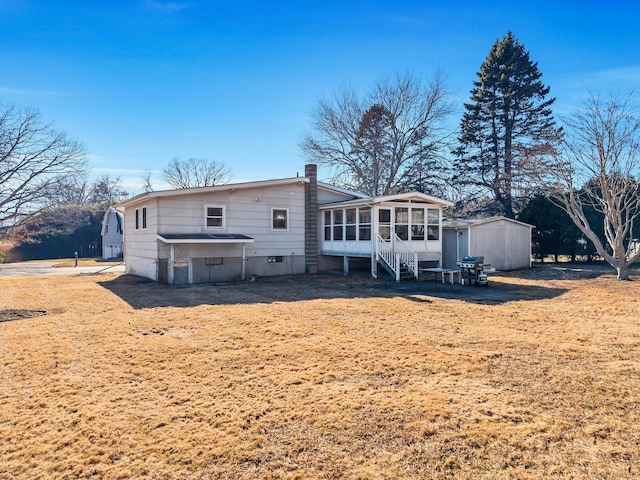 back of property featuring an outbuilding, a storage shed, a chimney, and a sunroom