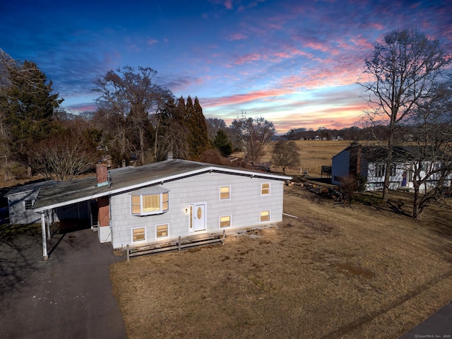 exterior space featuring a carport, driveway, a chimney, and a yard