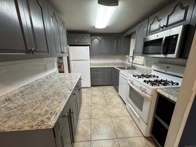 kitchen with light tile patterned floors, white appliances, a sink, backsplash, and gray cabinets