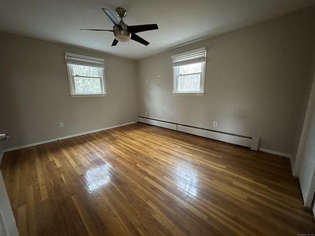 empty room featuring plenty of natural light, a baseboard radiator, and wood-type flooring