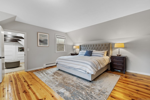 bedroom featuring lofted ceiling, baseboards, wood-type flooring, and a baseboard radiator