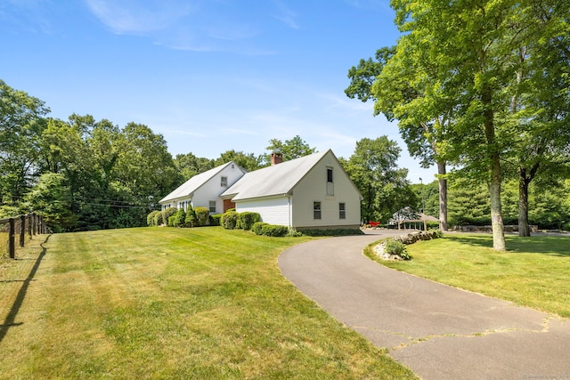 view of front facade featuring a front lawn, fence, driveway, and a chimney