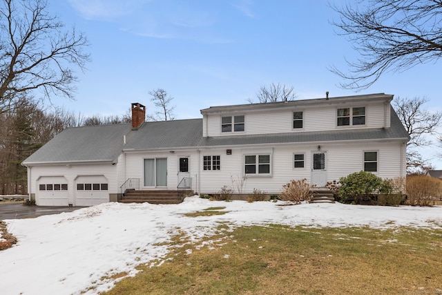 snow covered property with an attached garage and a chimney