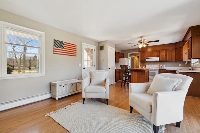 sitting room with a baseboard heating unit, light wood-type flooring, and ceiling fan