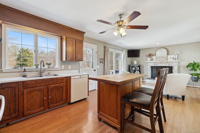 kitchen with a breakfast bar area, a fireplace, a sink, dishwasher, and light wood-type flooring