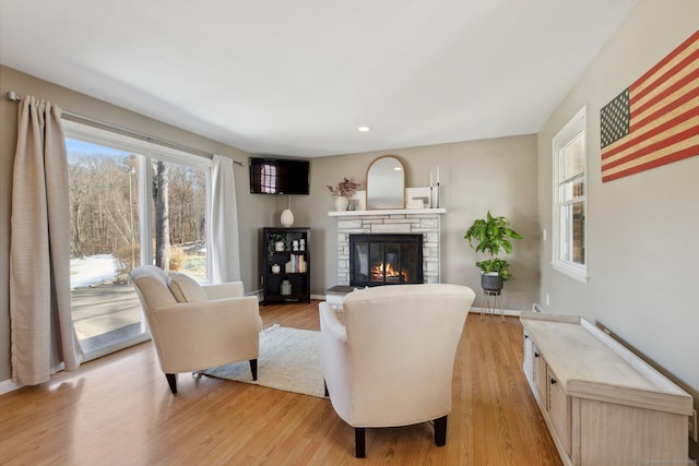 living area featuring a stone fireplace, recessed lighting, baseboards, and light wood finished floors