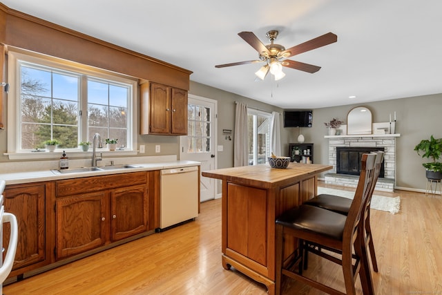 kitchen featuring light wood-type flooring, butcher block countertops, a sink, a stone fireplace, and white dishwasher