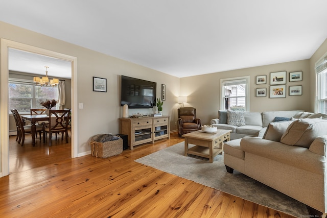 living area featuring an inviting chandelier, light wood-style floors, and baseboards