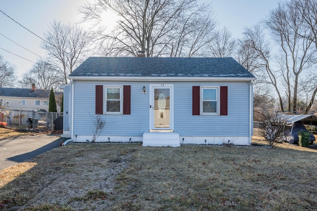 bungalow with a front lawn, fence, and a shingled roof