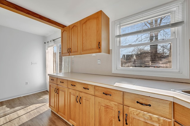 kitchen with light countertops, beamed ceiling, and light wood-style floors